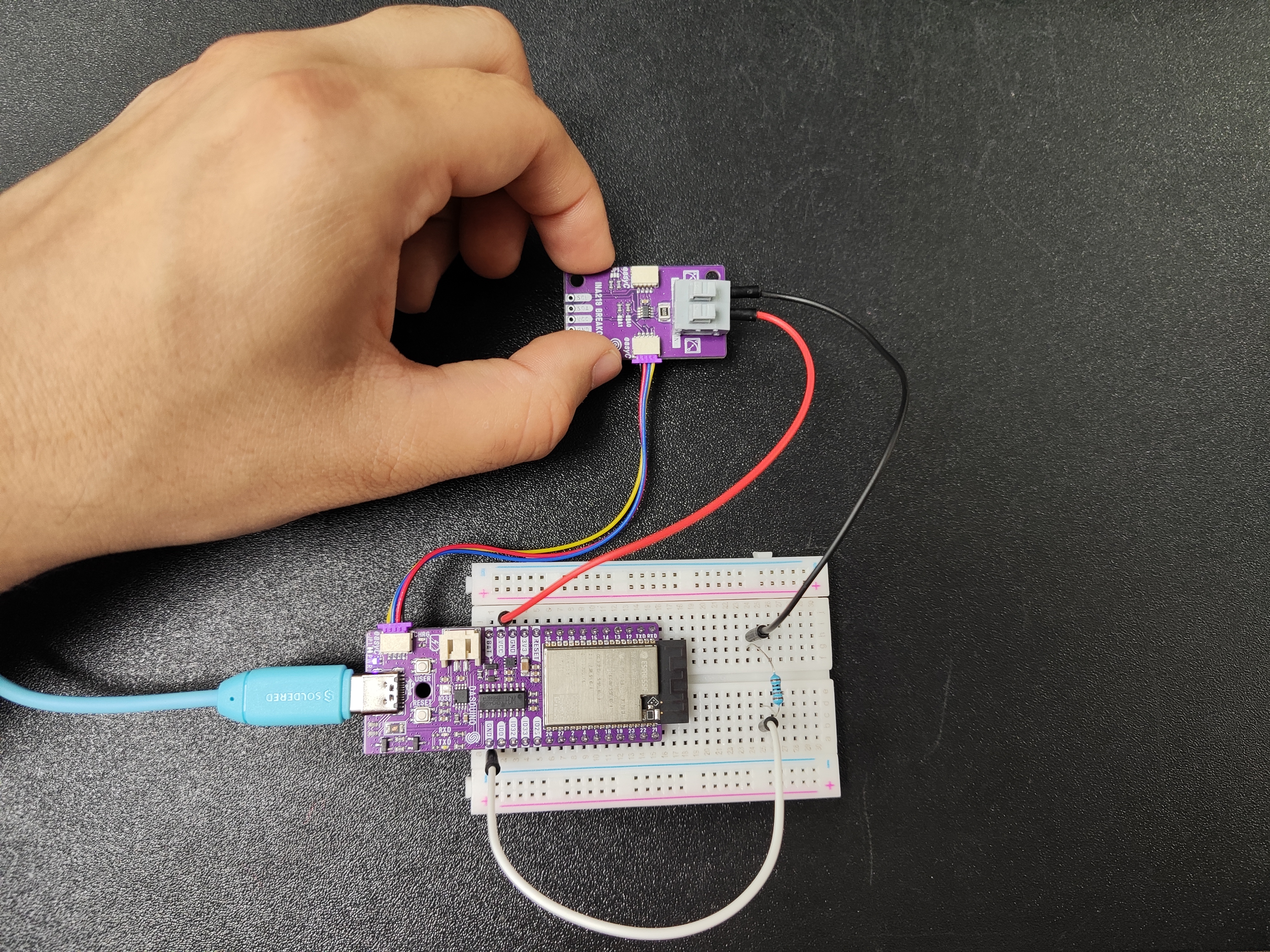 An INA219 current sensor breakout wired between a power supply and a load, with I2C going back to the development board