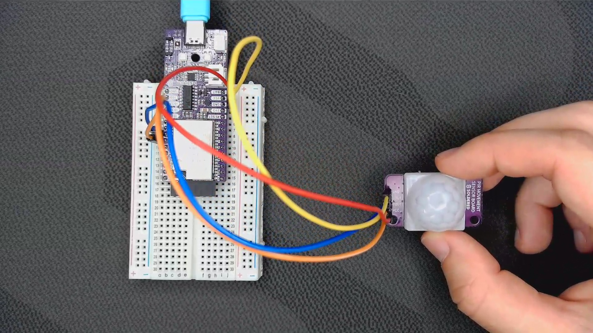 A PIR movement sensor board wired to a development board using three jumper wires for power, ground and the output pin